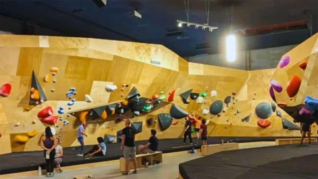Completed indoor bouldering gym with climbers practicing on colorful holds attached to angled wooden climbing walls and padded flooring