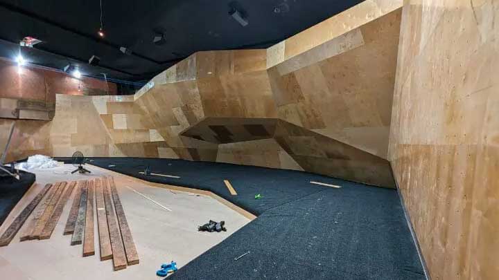 Indoor climbing gym under construction with wooden walls, scattered materials, and overhead lighting