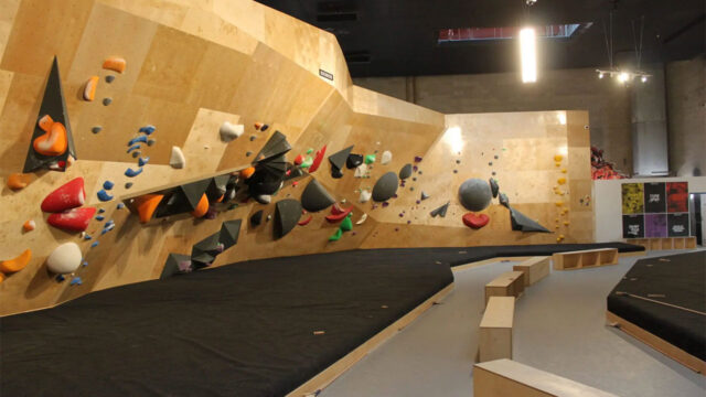 Indoor bouldering gym with colorful holds attached to angled wooden climbing walls and padded flooring