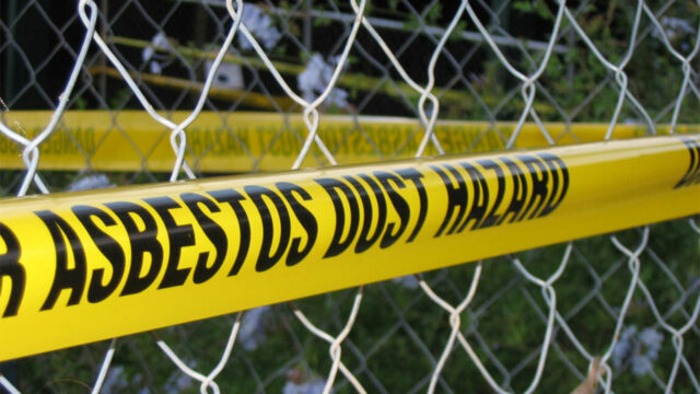 Yellow caution tape warning of asbestos dust hazard on a chain-link fence