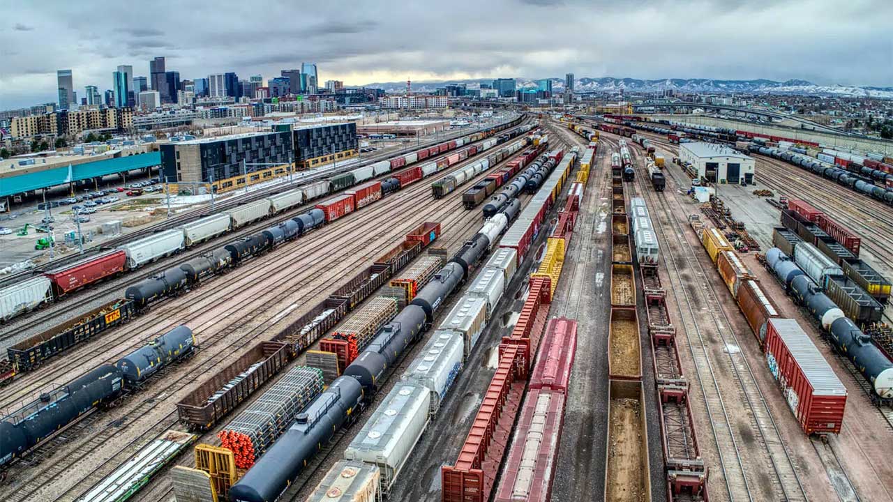Aerial view of extensive train yard with freight cars and city skyline in the background