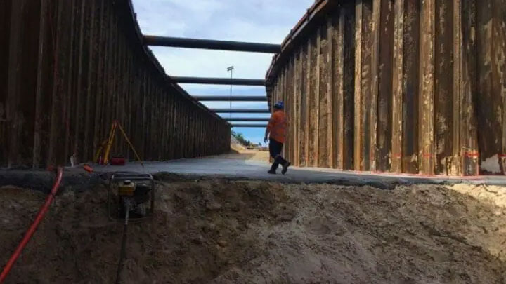 Construction worker walking inside a deep trench with steel sheet piling walls
