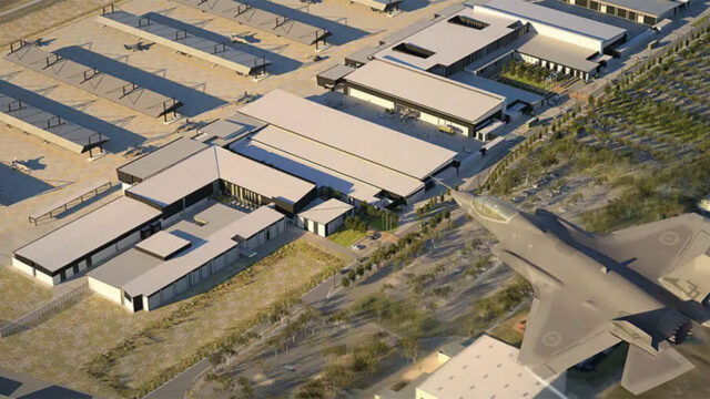 Aerial view of modern buildings and parked aircraft near a military jet flying overhead