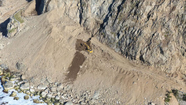 Aerial view of an excavator working on a rocky coastal slope near the ocean shoreline