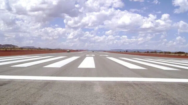 Close-up of an empty runway with white markings under partly cloudy sky in open landscape