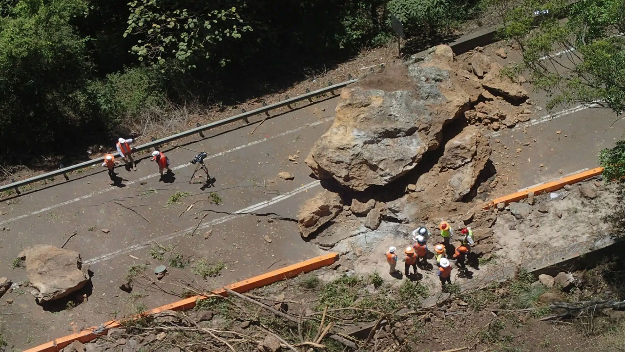 Aerial view of workers inspecting large boulders blocking a road after a landslide