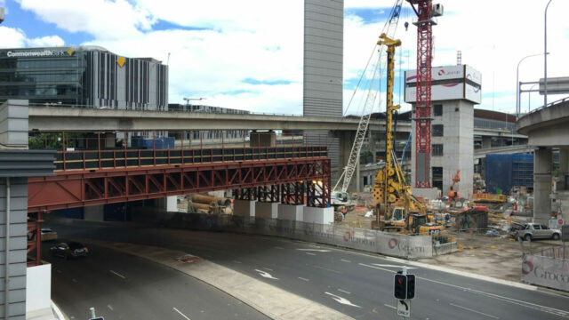 Urban construction site with cranes, scaffolding, and highway underpass near office buildings