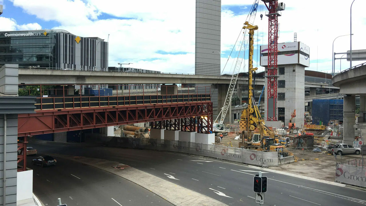 Urban construction site with cranes, scaffolding, and highway underpass near office buildings