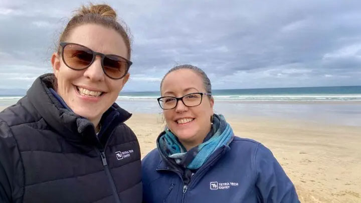 Close up photo of Katie Watt (left) and Erin Pears (right) on a boardwalk in front of a ocean shoreline