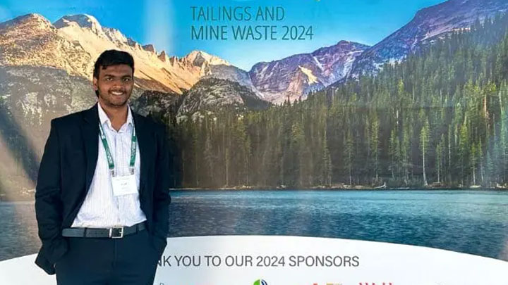 Nilan Jayasiri standing in front of a banner backdrop with mountains, lake, and text that reads "Tailings and Mine Waste 2024"
