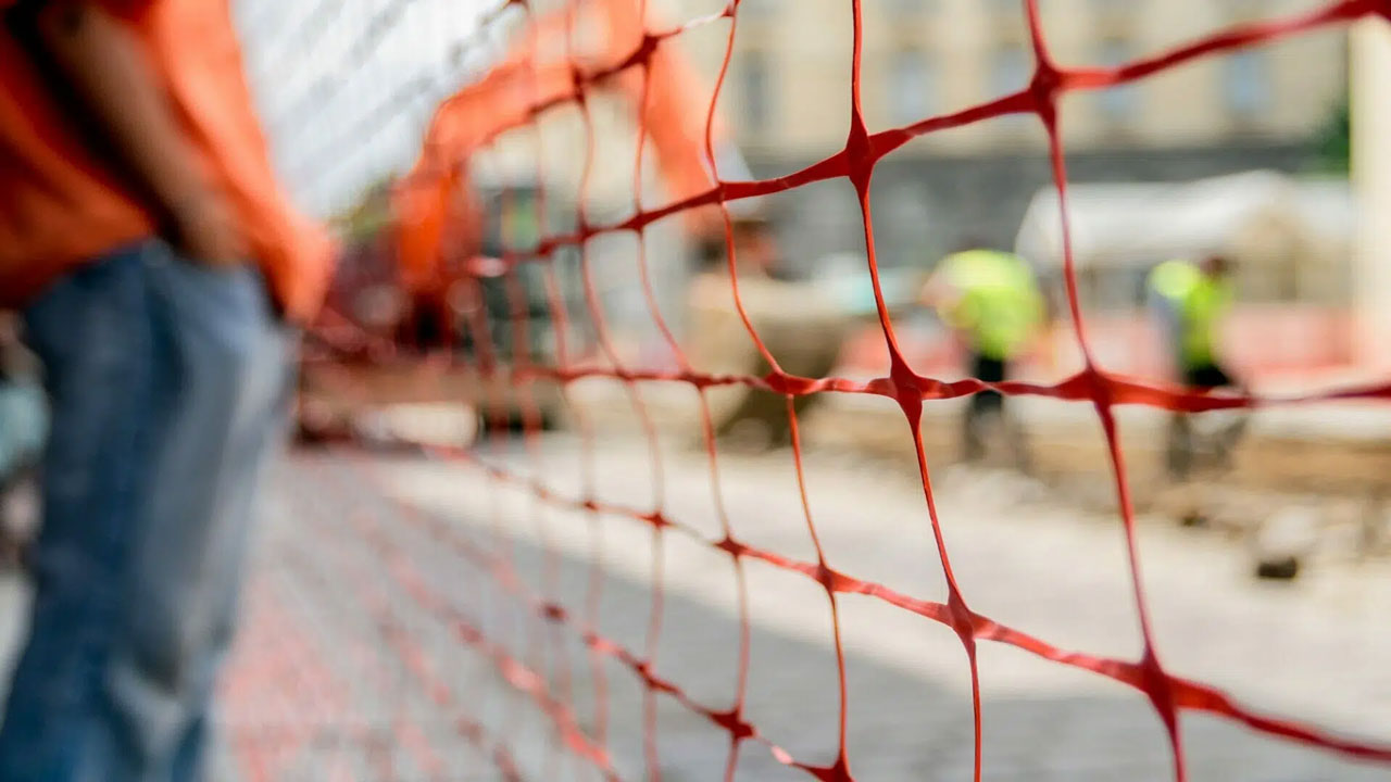 Close-up of orange construction safety net with blurred workers