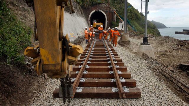 A construction site with heavy machinery and workers building railway tracks on a dirt and gravel terrain