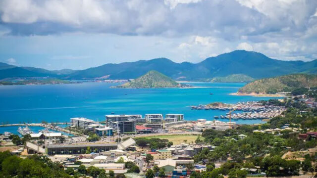Coastal view of Port Moresby with buildings, marina, and mountains under a partly cloudy sky