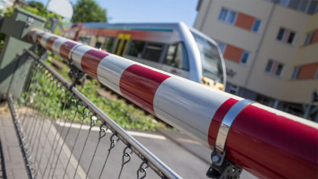 A red and white striped barrier blocks a railway crossing as a train approaches