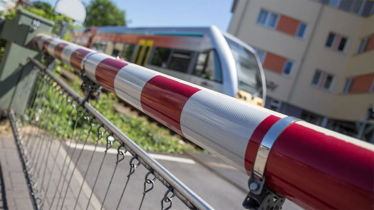 A red and white striped barrier blocks a railway crossing as a train approaches