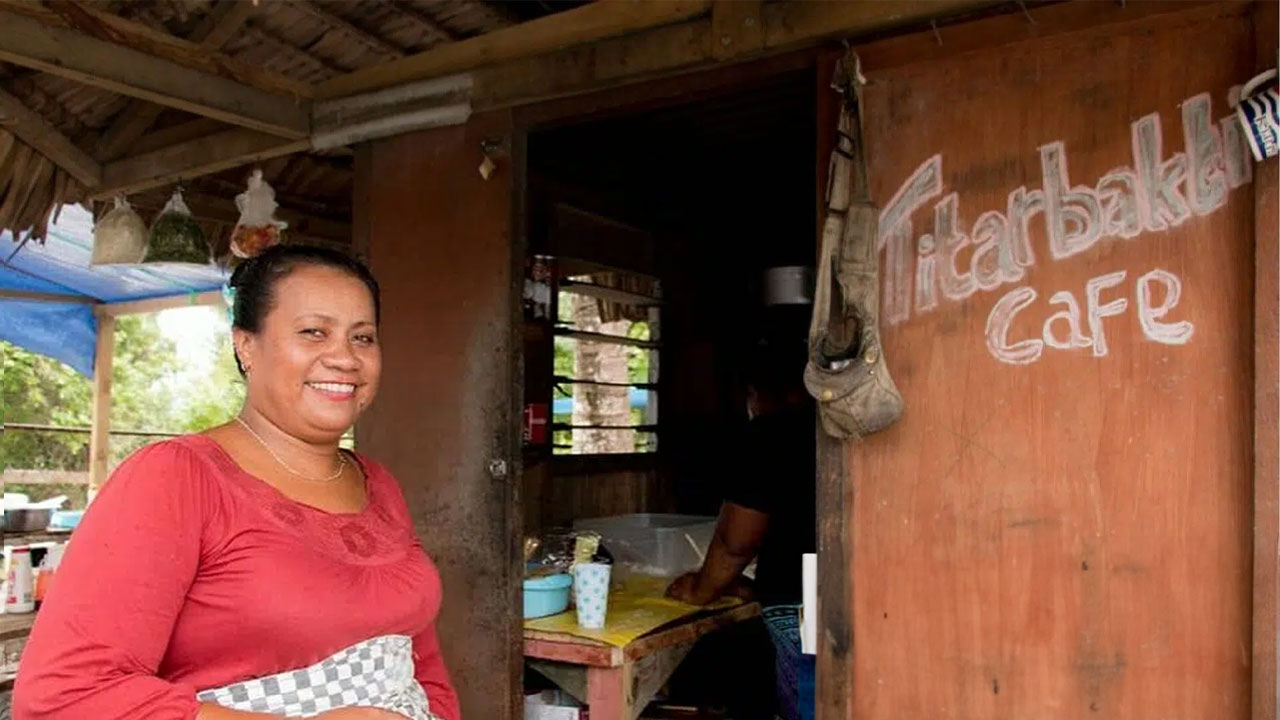 Woman smiling outside rustic café with "Titarbakki Café" written on wooden wall.